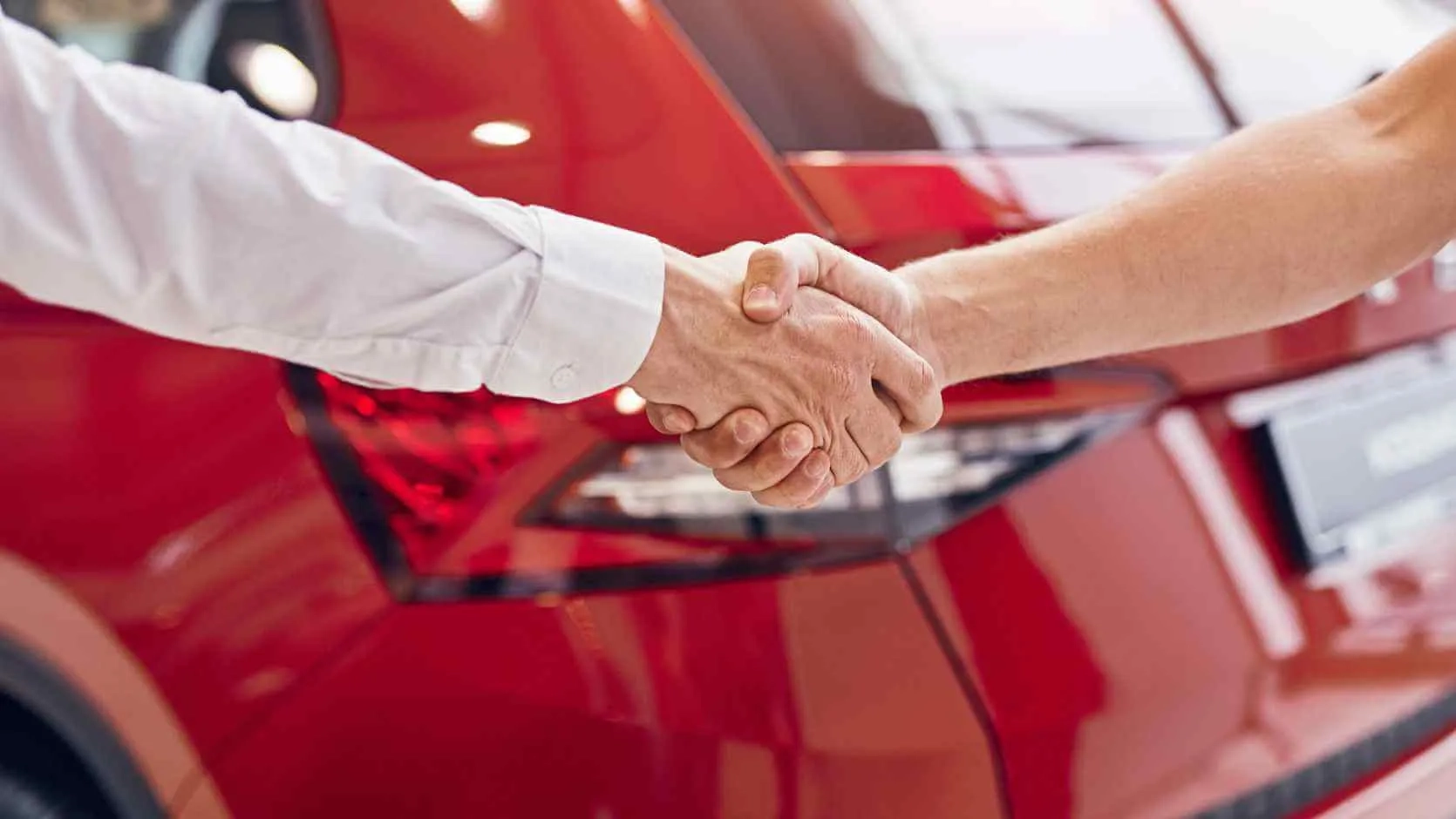 Handschlag vor einem roten Fahrzeug im Autohaus