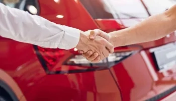 Handschlag vor einem roten Fahrzeug im Autohaus